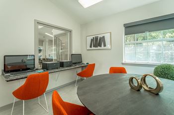 a conference room with a round table and orange chairs and a computer desk